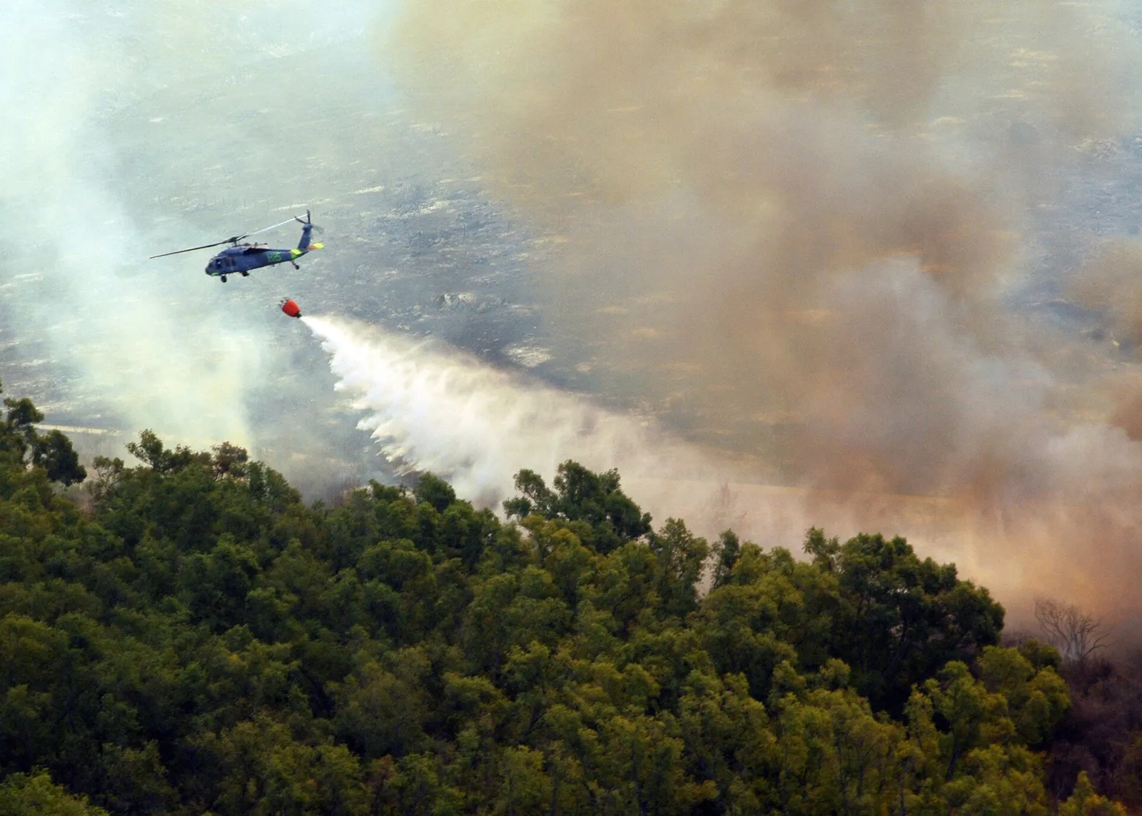 En helikopter fäller vatten över en skogsbrand